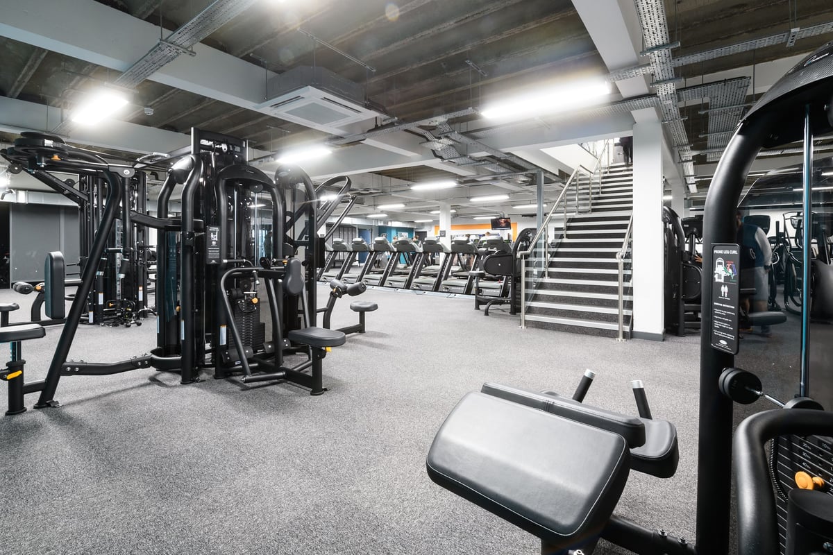 PureGym Brighton London Road: Resistance machines, weight benches, dumbbells, and cardio equipment in a dimly lit gym space.