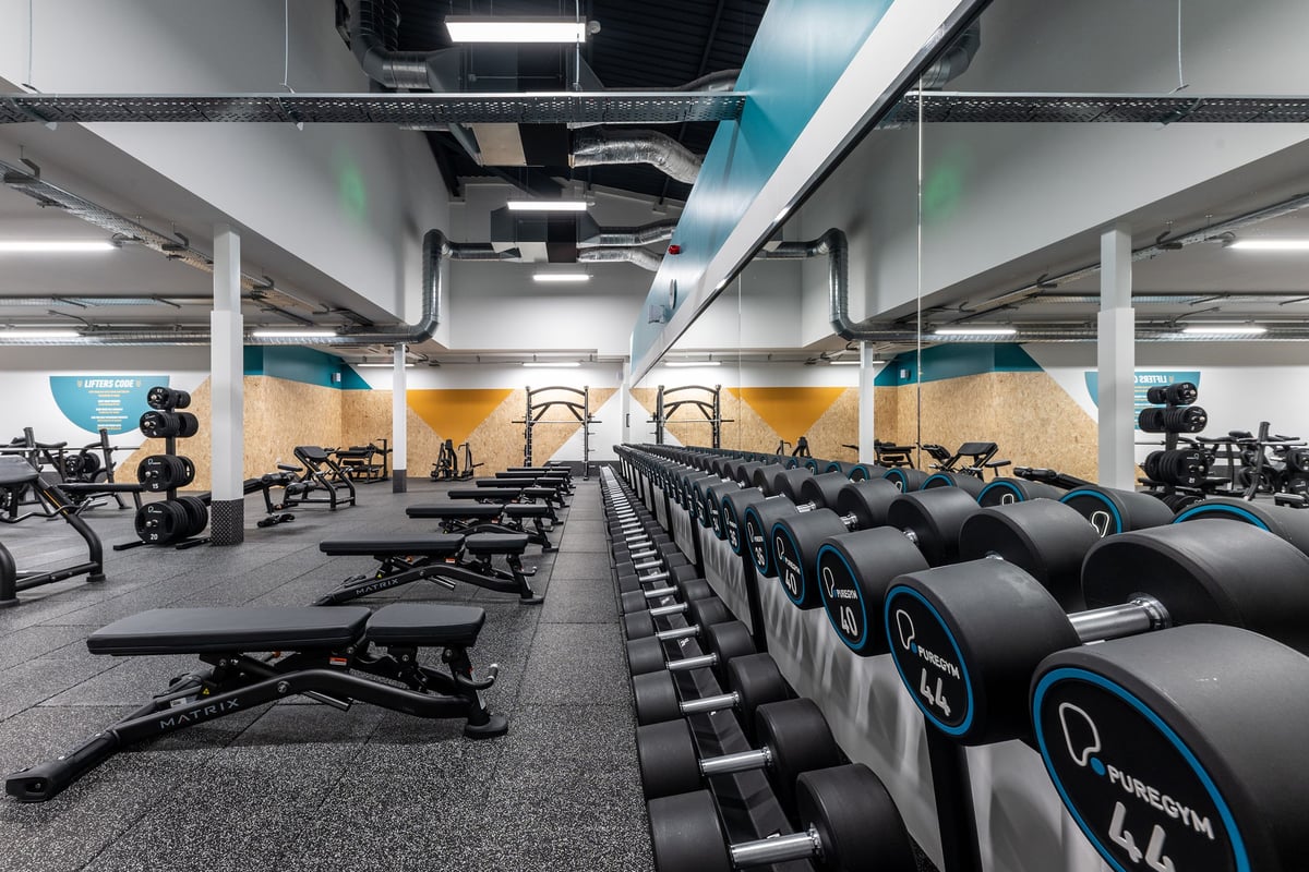 PureGym Redditch Ringway: Rows of workout benches, free weights, rubberized flooring in a gym with mirrored walls.