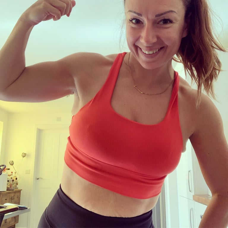 Woman in red sports bra flexing arm and smiling in kitchen