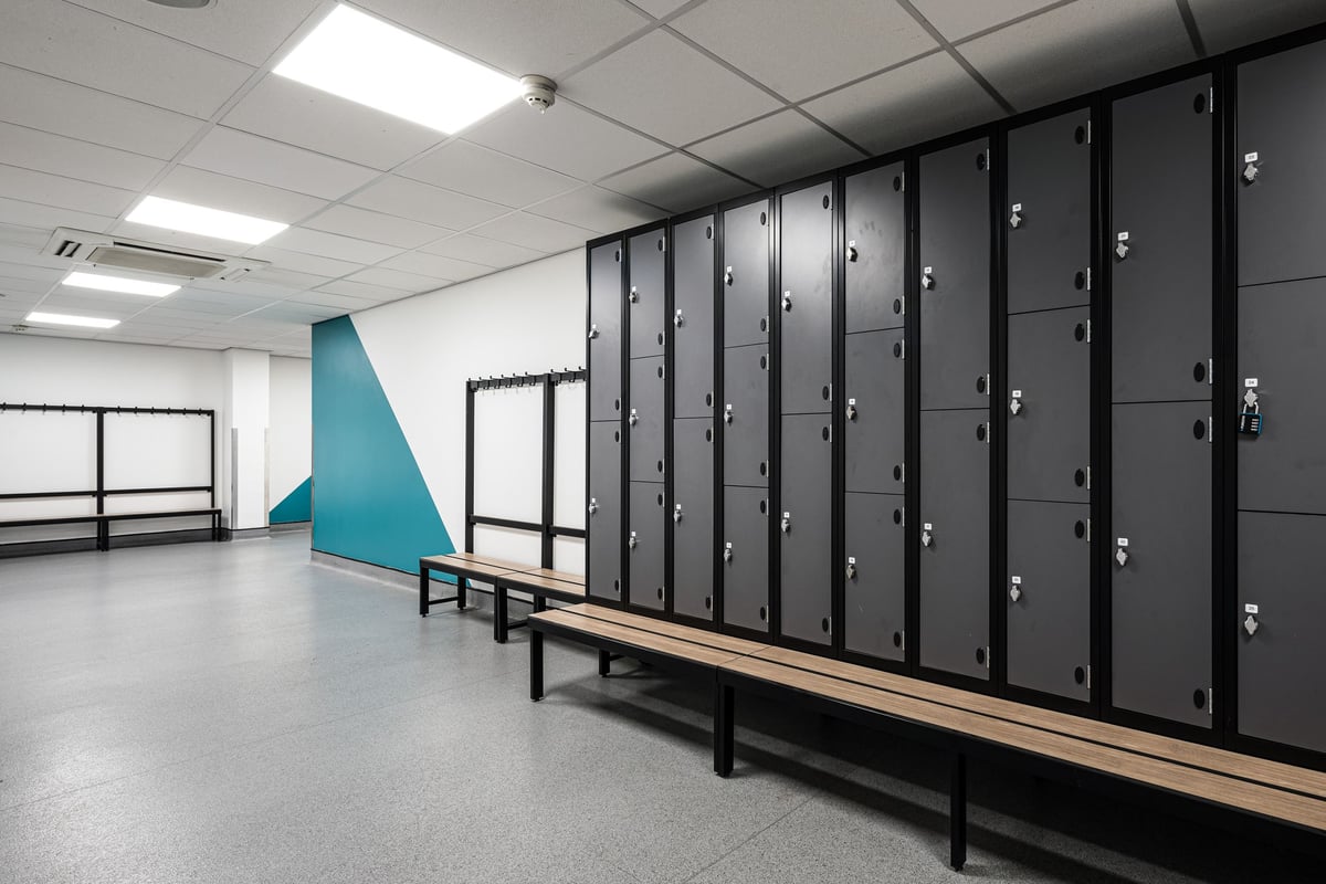 PureGym Dudley Tipton: Rows of lockers, bench seating and geometric wall design in a changing room.