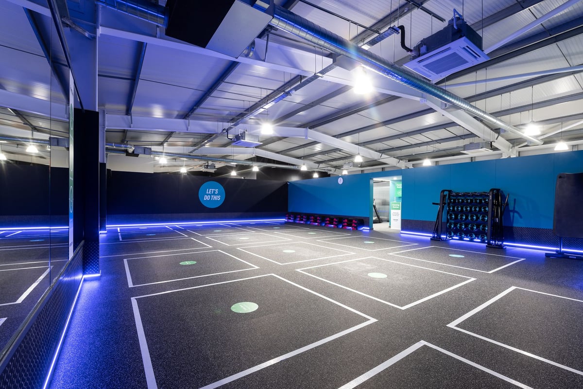 PureGym Andover: Indoor basketball court, blue-lit with markings on rubberized flooring and benches.