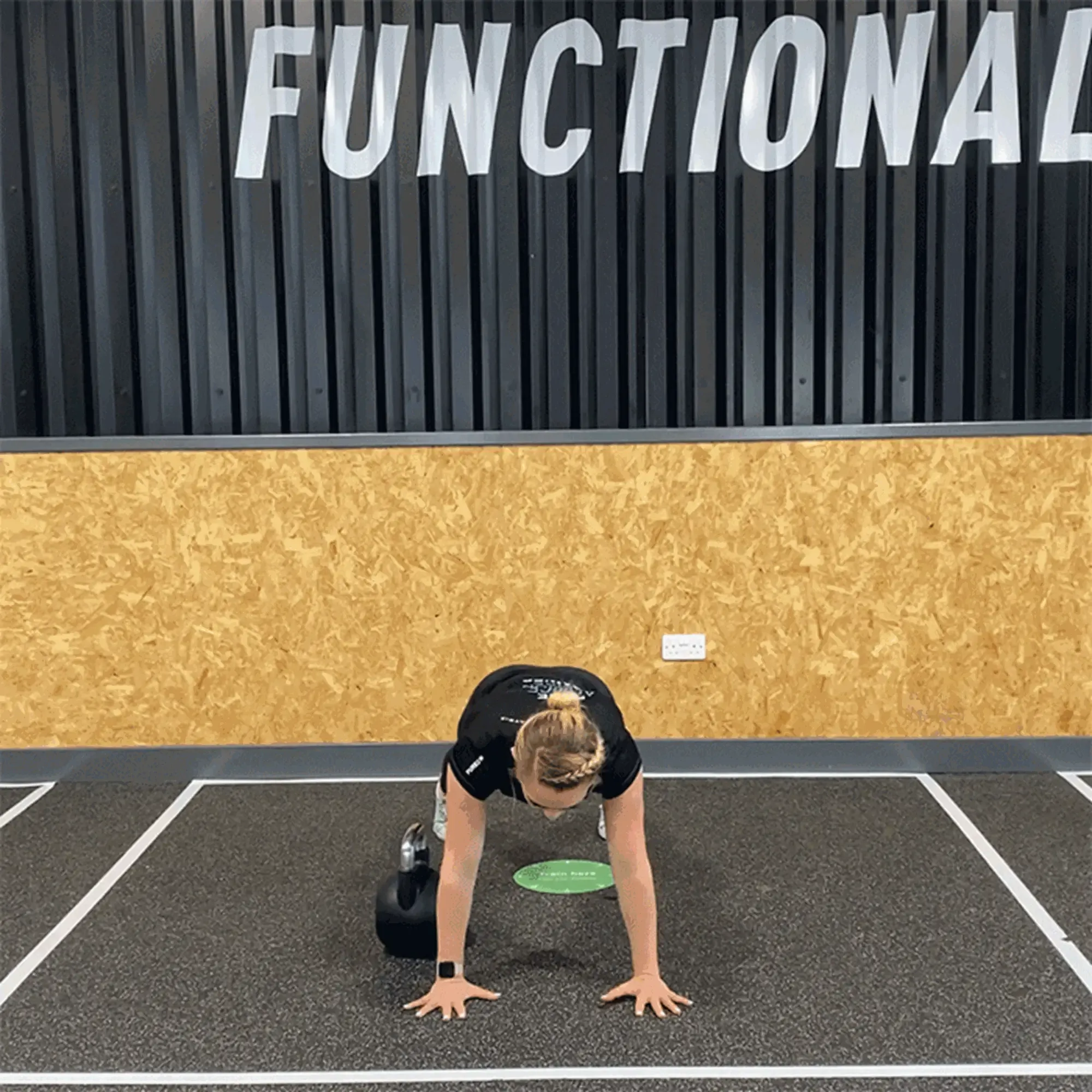 Woman in plank position with one knee on kettlebell in gym marked area