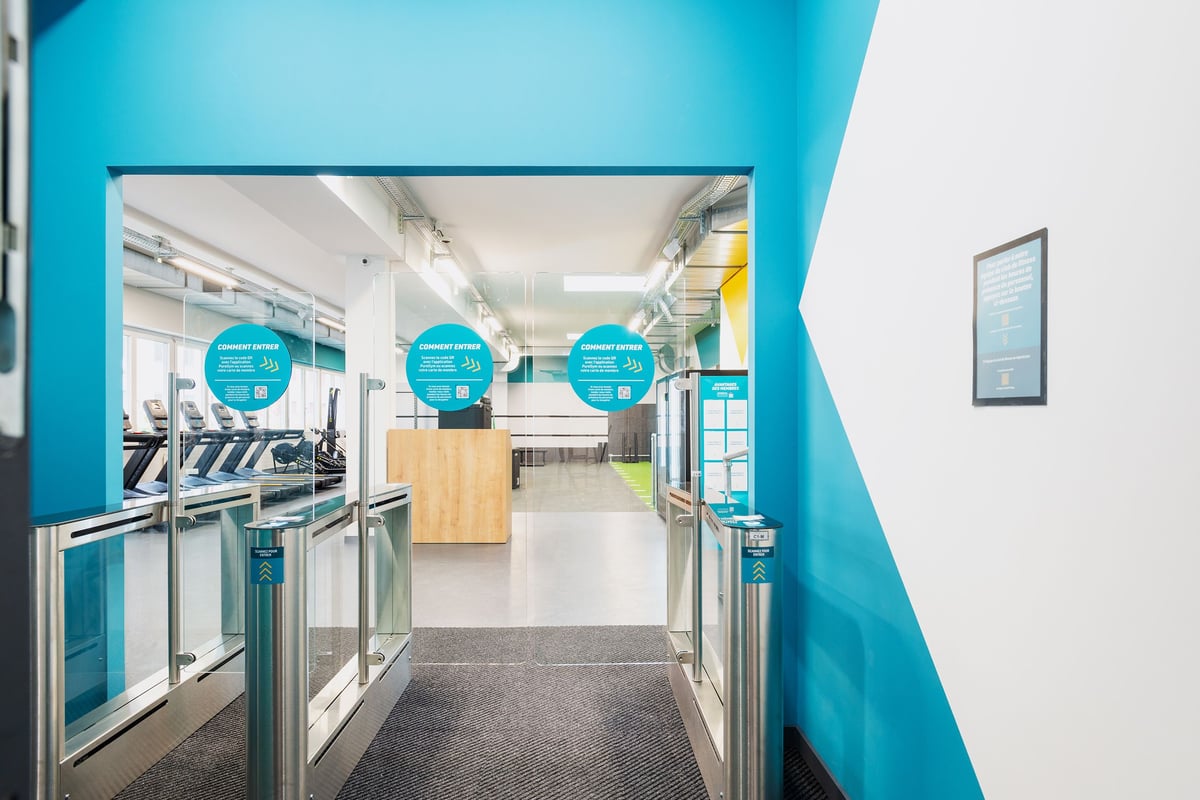 PureGym Vevey: Des rangées de machines de cardio-training à l'intérieur d'un espace lumineux avec des murs d'accent bleu sarcelle et une signalisation circulaire.