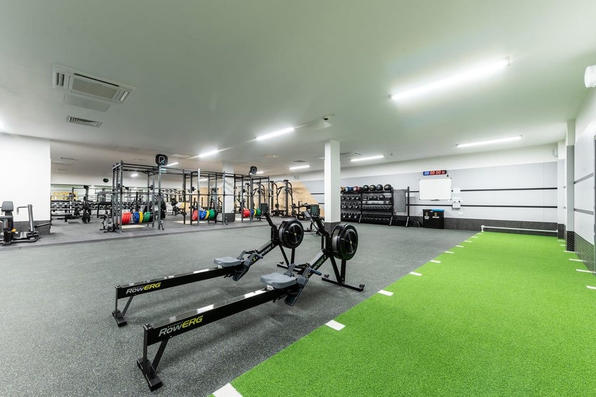 PureGym Tyldesley: Functional training area with squat racks, barbells, weight plates, turf zone, and rubberized flooring.