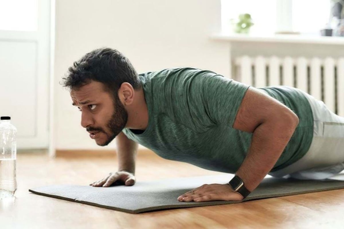 Mann führt Plankenübung auf Yogamatte in hellem, minimalistischem Raum mit Wasserflasche a