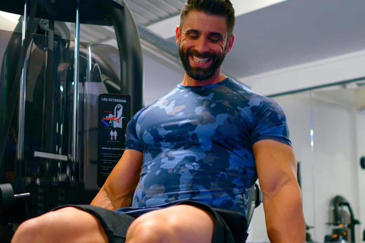 Man in blue camo shirt smiling while using leg extension machine at gym