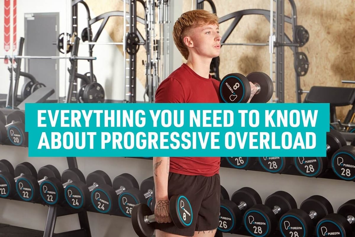 Young man lifting dumbbells in gym with weights on racks behind him