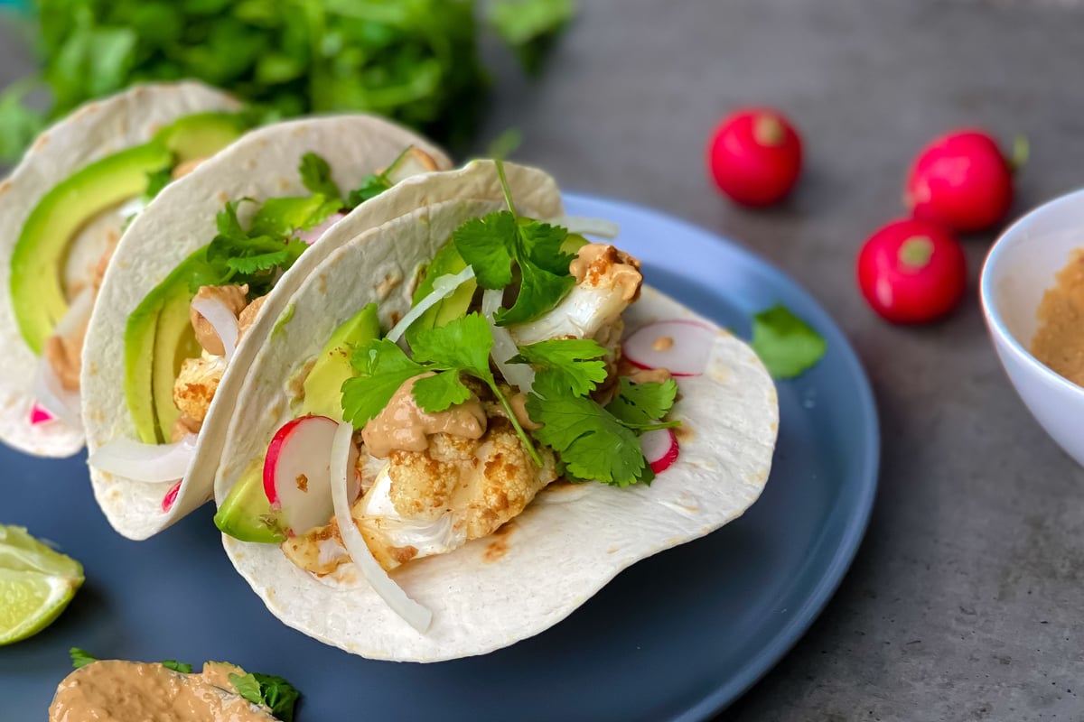 Soft tacos filled with cauliflower, avocado, radish and coriander on a blue plate