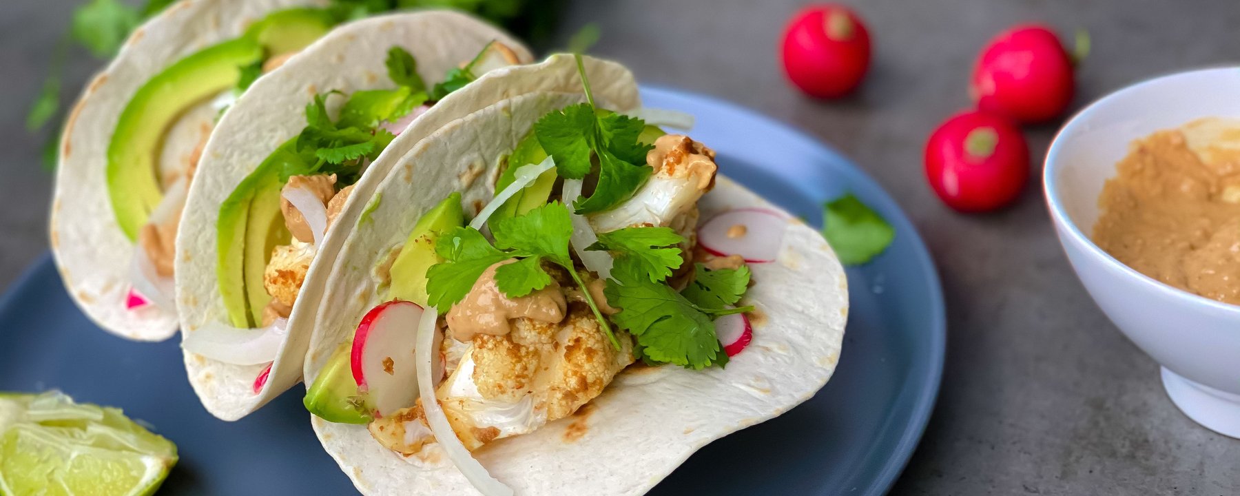 Soft tacos filled with cauliflower, avocado, radish and coriander on a blue plate