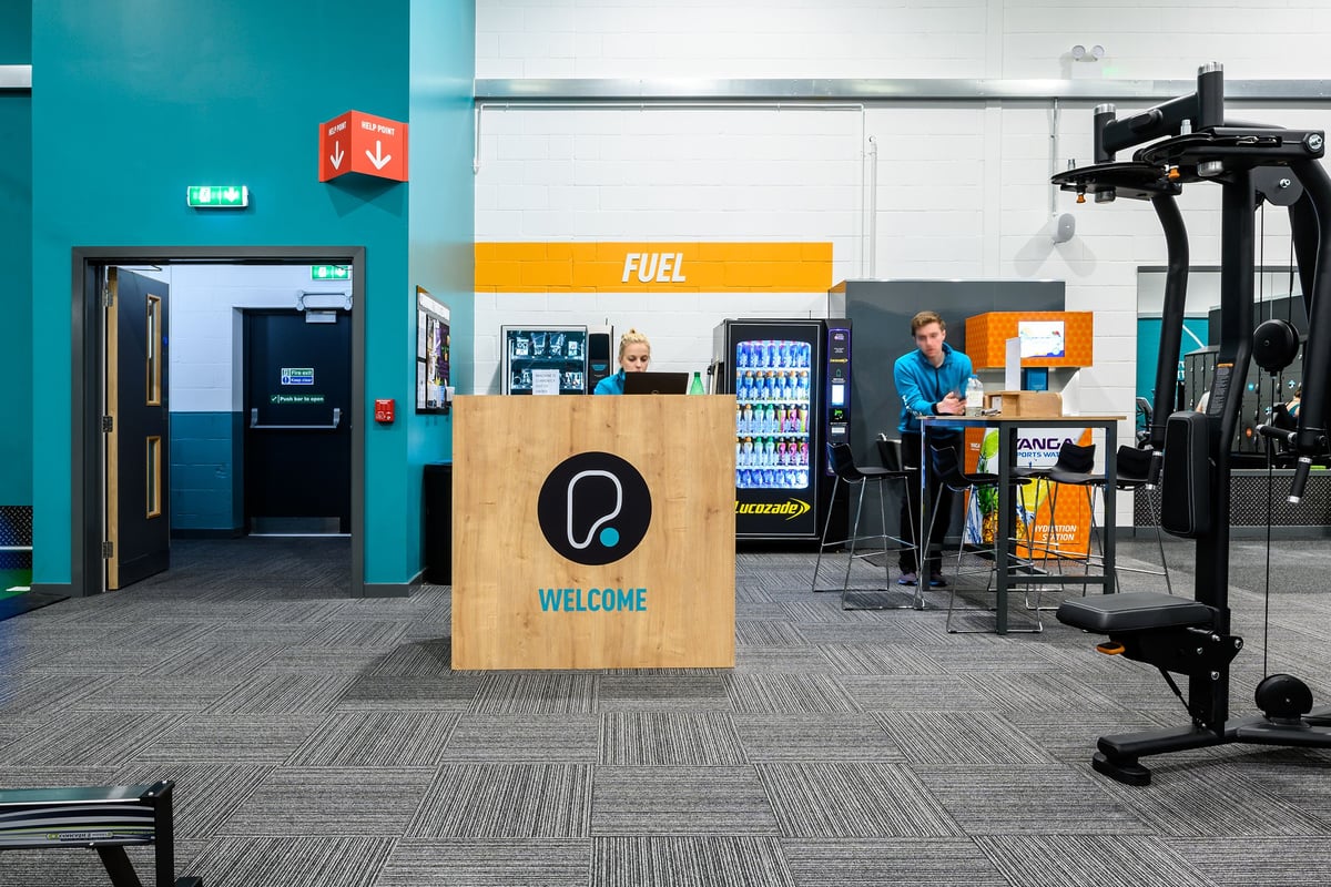 PureGym Burgess Hill: Gym entrance with vending machines, seating area, and fitness equipment.