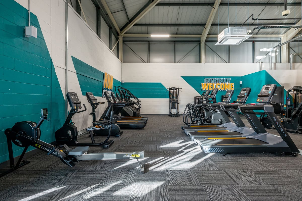 PureGym Oswestry: Rows of treadmills, ellipticals, and exercise bikes in a teal-accented gym interior.