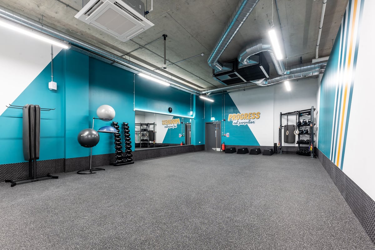 PureGym London Feltham: Weights, resistance machines, rubber flooring, teal accents, open layout with mirrors on one wall.