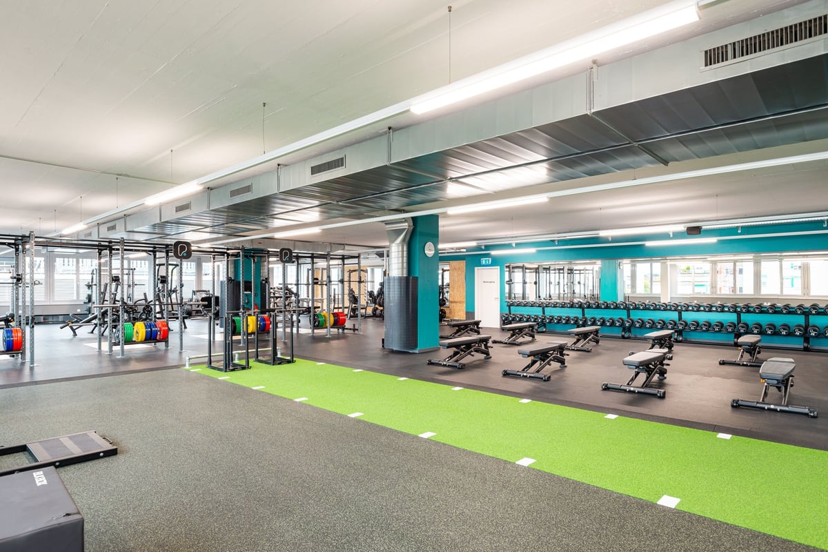 PureGym Altstetten: Grosszügiger Fitnessbereich mit Krafttrainingsgeräten, Kardiogeräten und Grünrasenzone.