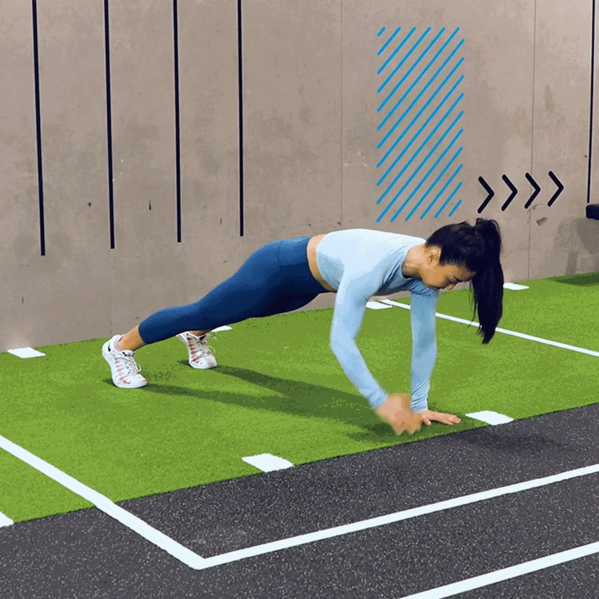 Woman in blue workout clothes doing a plank exercise on green turf indoors