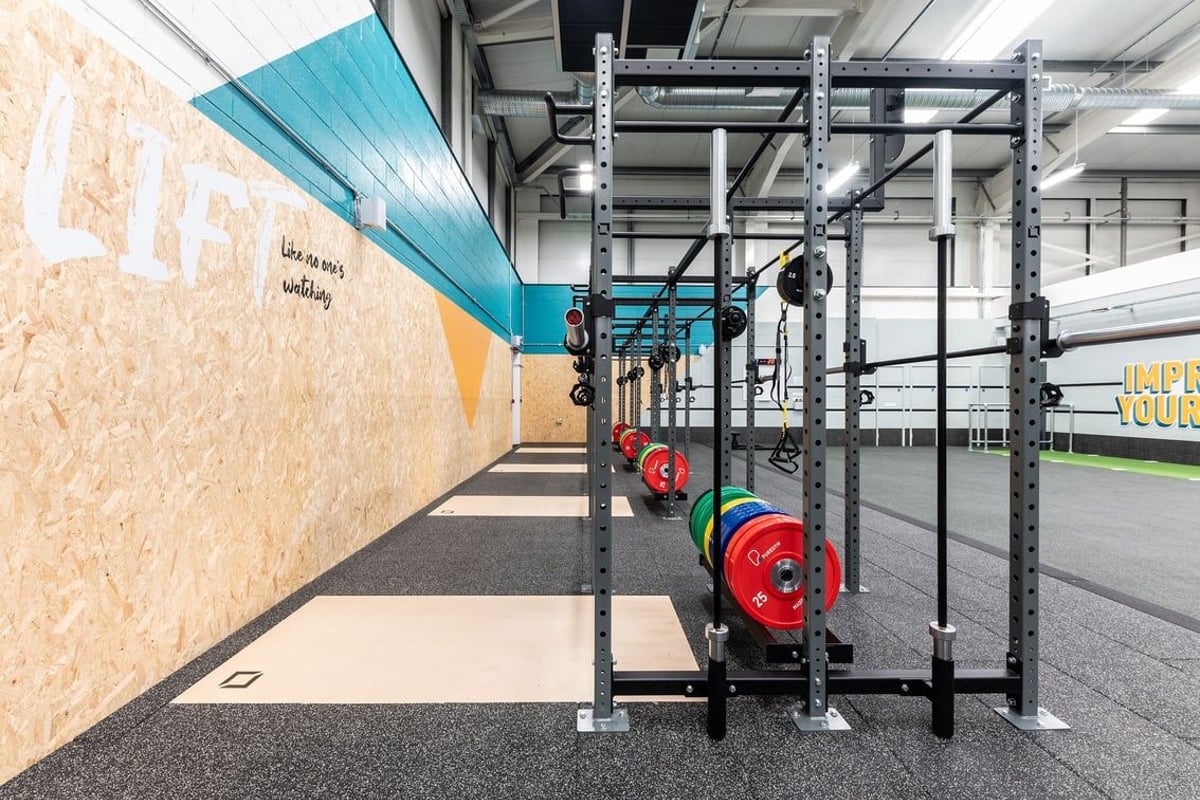 PureGym Sheffield Crystal Peaks: Gym room with weight racks, weights, bars, and rubberized flooring along teal accent wall.