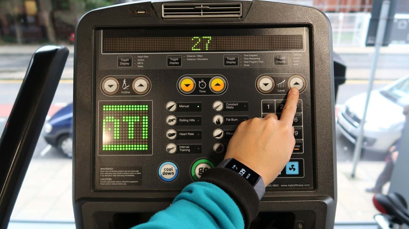 Hand pressing level up button on treadmill control panel with digital display showing 27