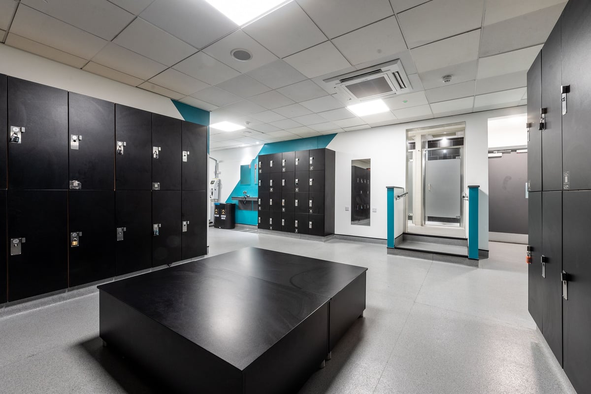 PureGym Loughborough: Rows of lockers, benches in grey tones with teal accents, minimal design.