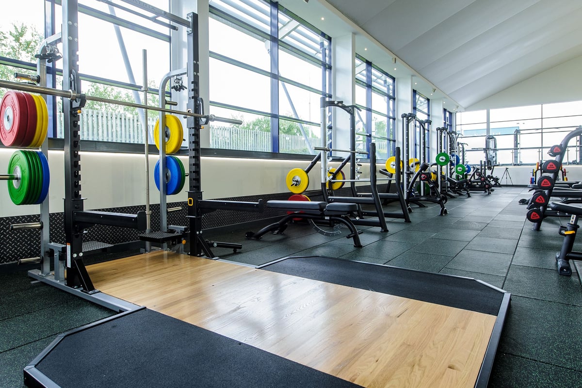 PureGym Denton: Weight racks, rubberised flooring, colourful weight plates, and benches in a bright gym space.