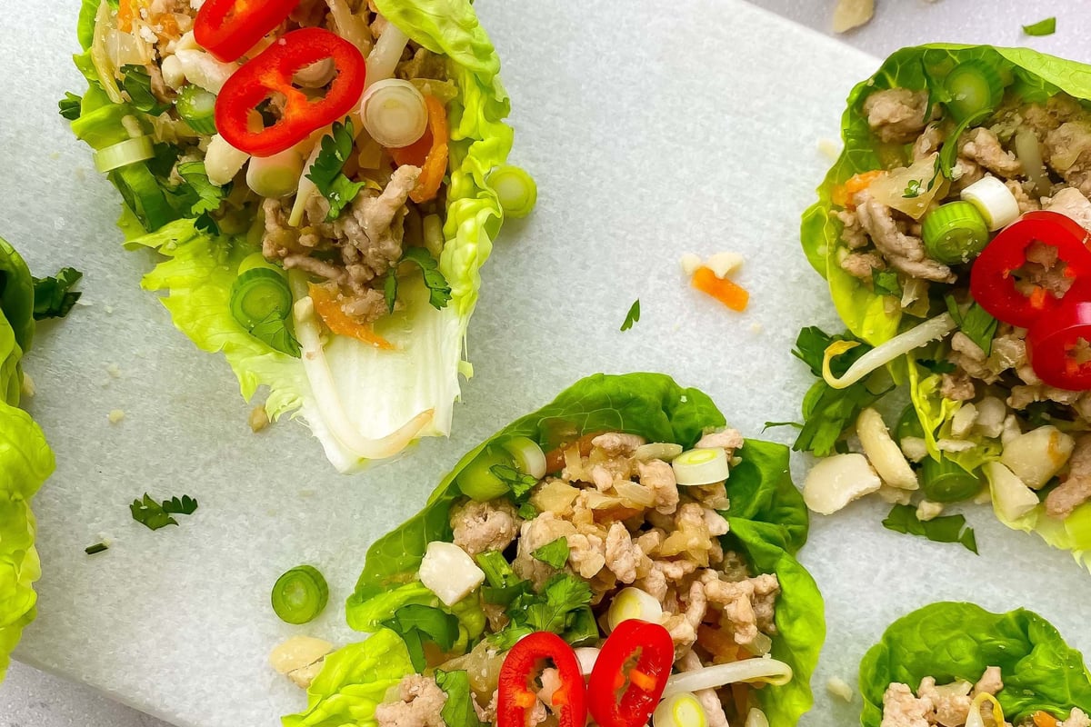 Lettuce wraps filled with minced meat, sliced red chili, spring onions, and herbs on a boa