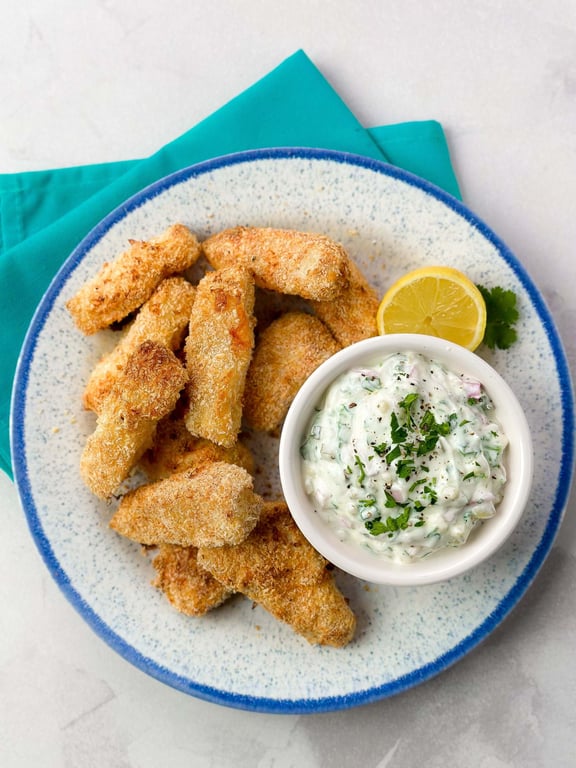 Breaded fish sticks with creamy herb dip and lemon wedge on a blue-rimmed plate