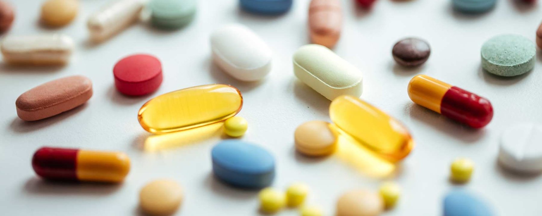 Différentes pilules et capsules colorées éparpillées sur une surface blanche