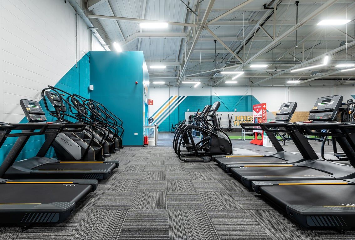 PureGym Taunton: Rows of treadmills, high ceilings, teal walls, and rubberized tiled flooring.