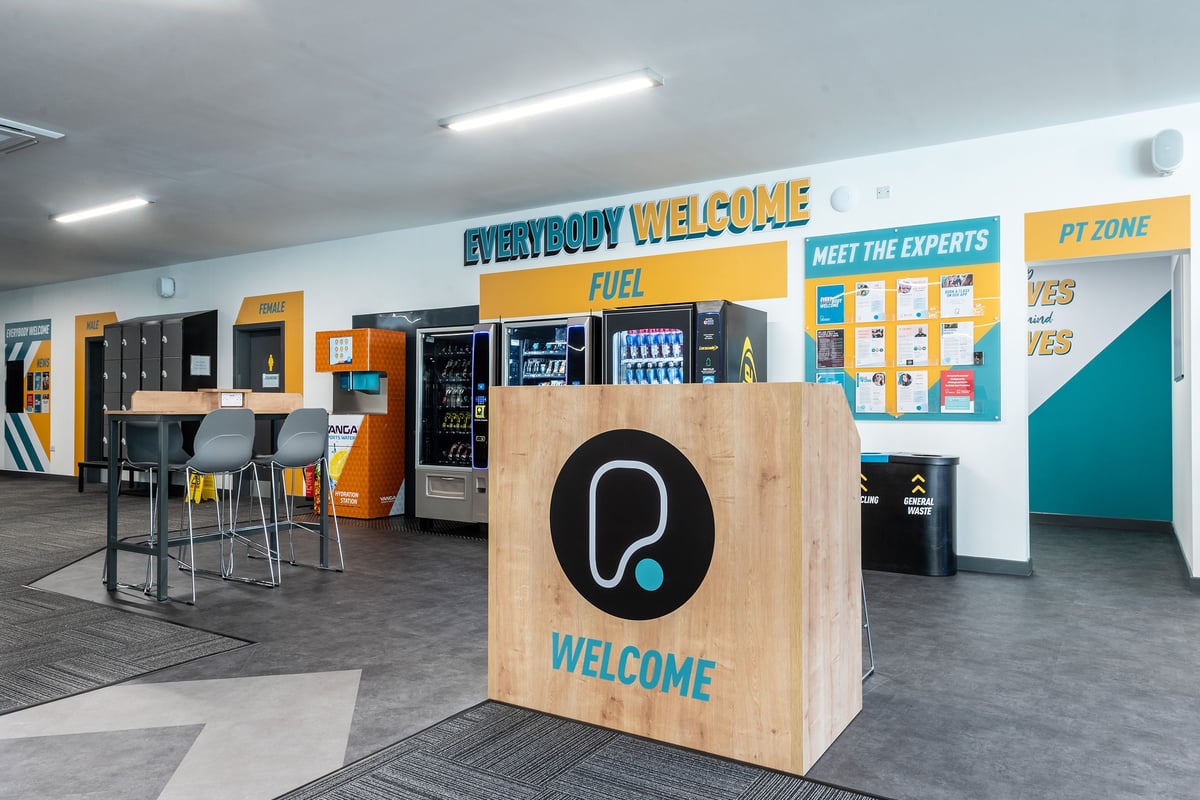 PureGym Tyldesley: Welcome area with vending machines, seating, informational displays, and personal training zone entrance.