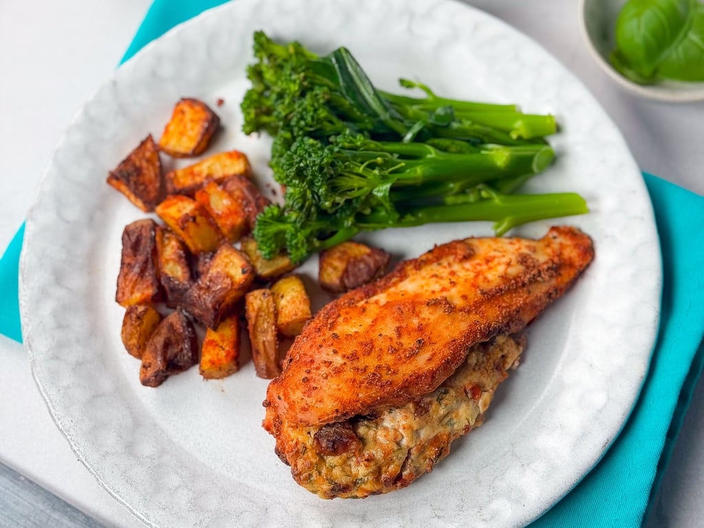 Stuffed chicken breast with roasted potatoes and steamed broccolini on a white plate
