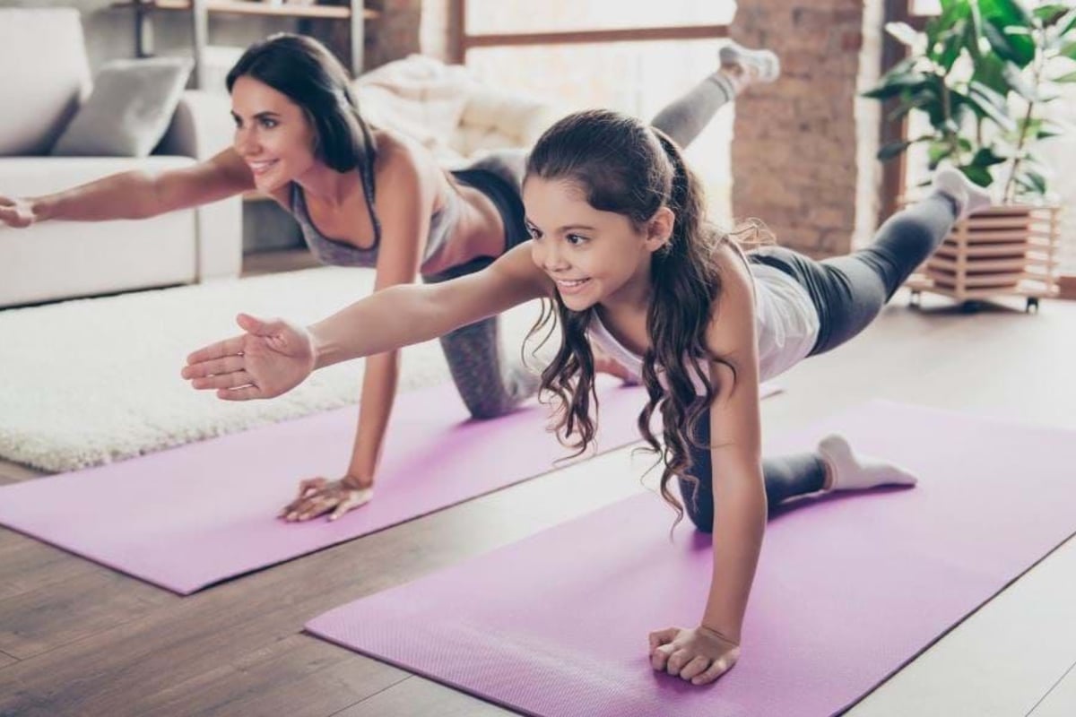 Woman and girl doing yoga stretches on mats in a bright living room