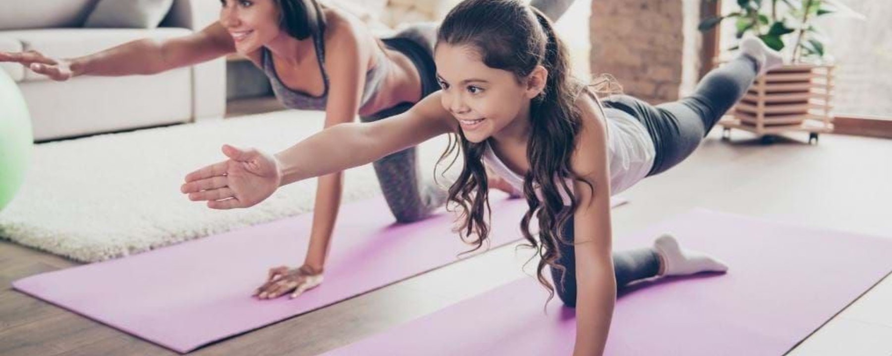 Woman and girl doing yoga stretches on mats in a bright living room