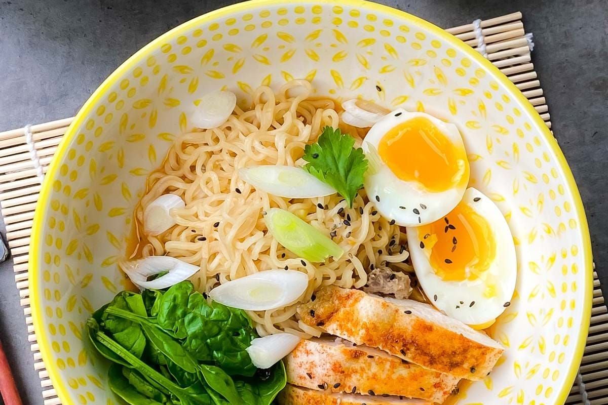 Ramen noodles with boiled eggs, grilled chicken, spinach, spring onions, and sauce bowl