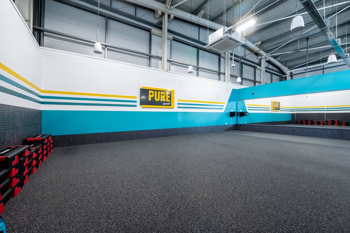 PureGym Stamford: Rubberized flooring, striped walls in the studio with stacks of step platforms opposite a mirrored wall.