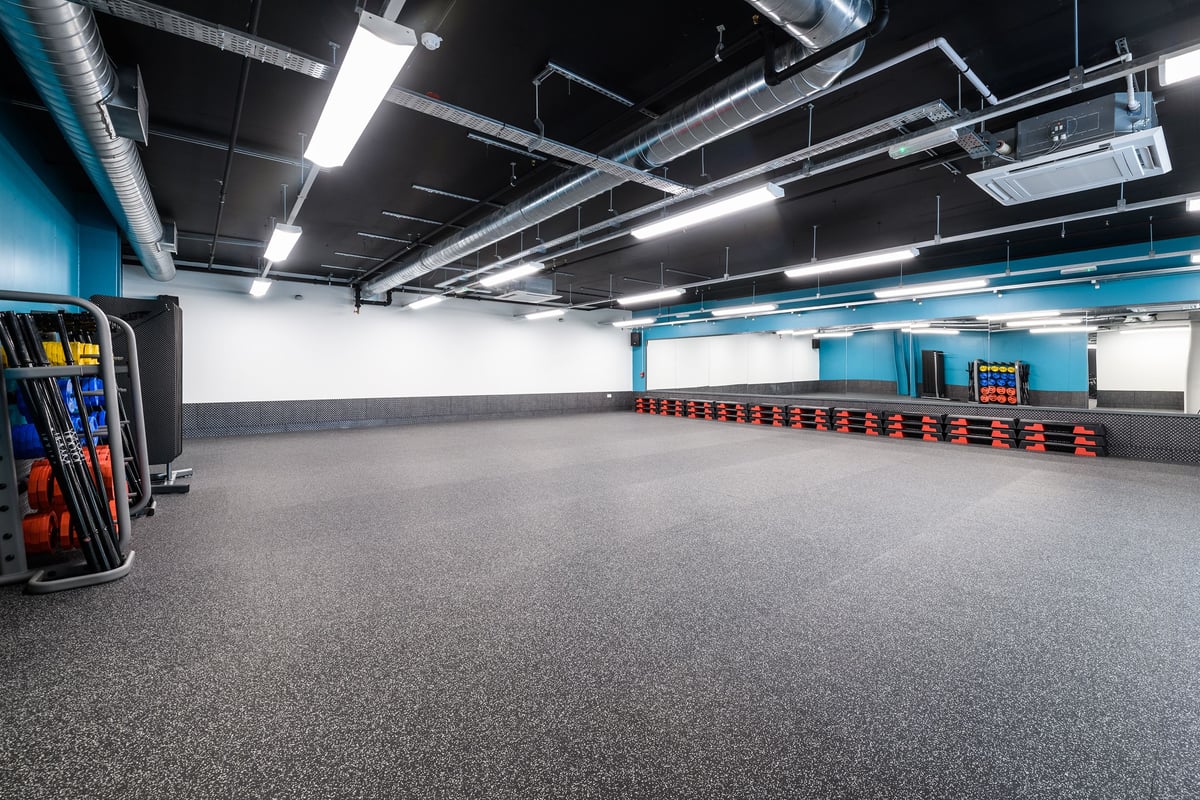 PureGym Glasgow Silverburn: Open gym floor with weight racks, rubberized flooring, and industrial lighting fixtures overhead.