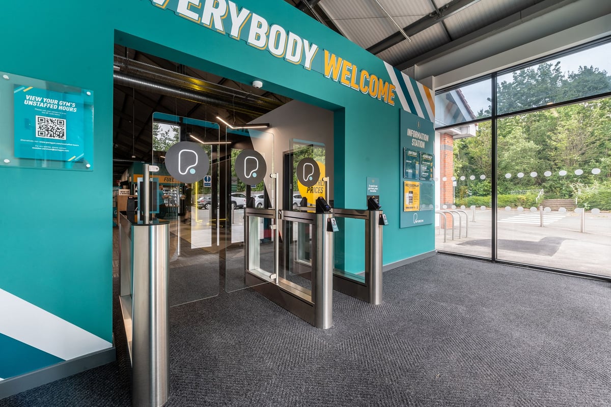 PureGym Derby Meteor Centre: Entrance area with turnstiles, "Everybody Welcome" signage, and floor mats.