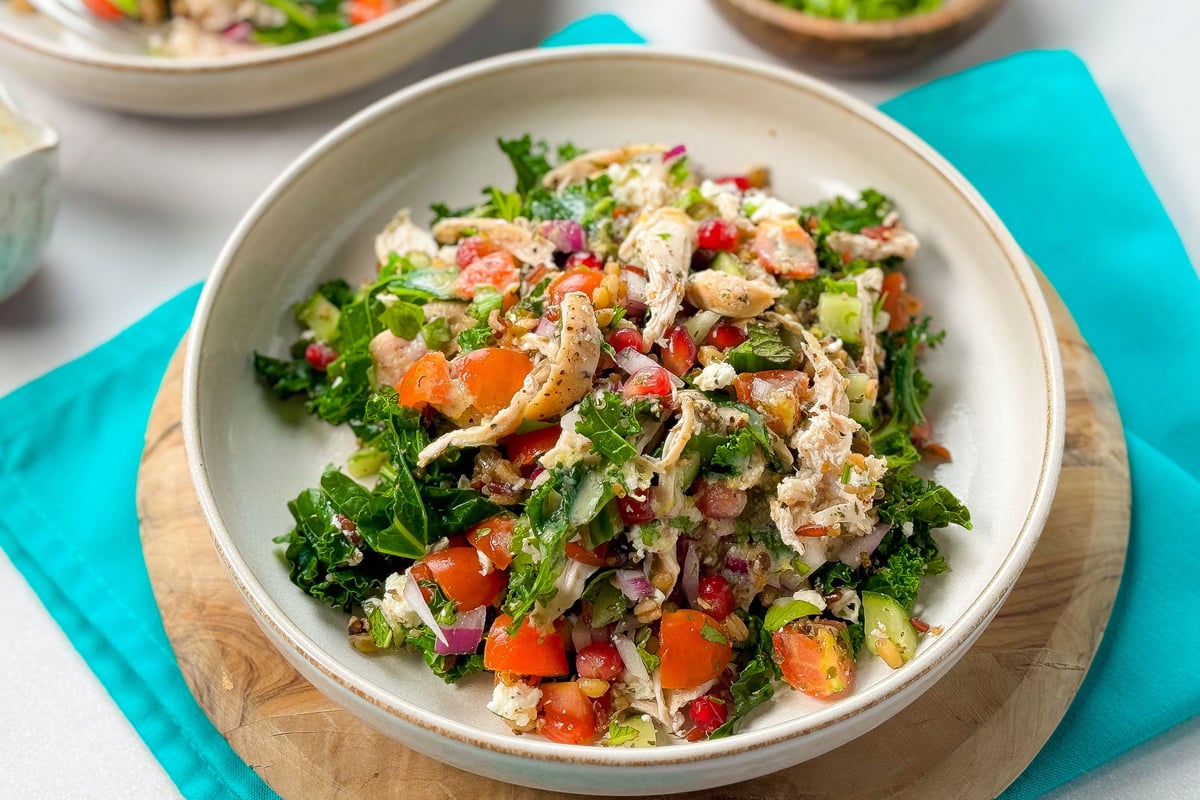 Herby chicken salad with kale, peppers, quinoa and tahini dressing in white bowl