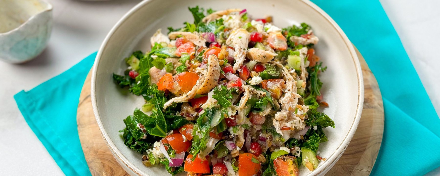 Herby chicken salad with kale, peppers, quinoa and tahini dressing in white bowl