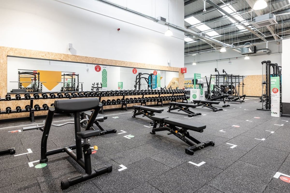 PureGym Stockport North: Rows of benches, free weights, rubberized flooring, and weight racks for strength training.