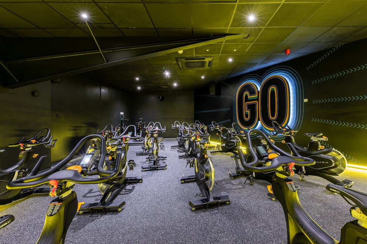 PureGym Brierley Hill: Rows of futuristic stationary bikes in neon-lit studio space with mirrored walls.