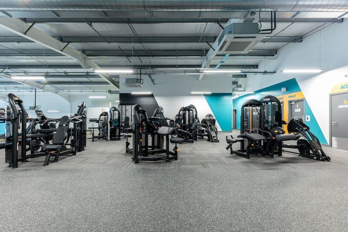 PureGym Liverpool Edge Lane: Resistance machines, benches, rubberized flooring in a gym studio with exposed ceiling ducts.