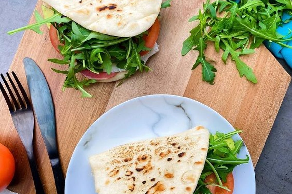 Two flatbread sandwiches with arugula and tomato on a wooden board and plate