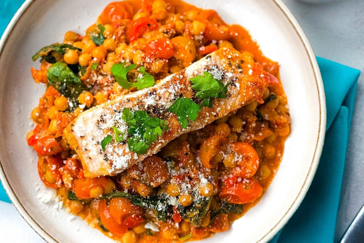 Grilled salmon on chickpea and spinach stew garnished with parsley and cheese
