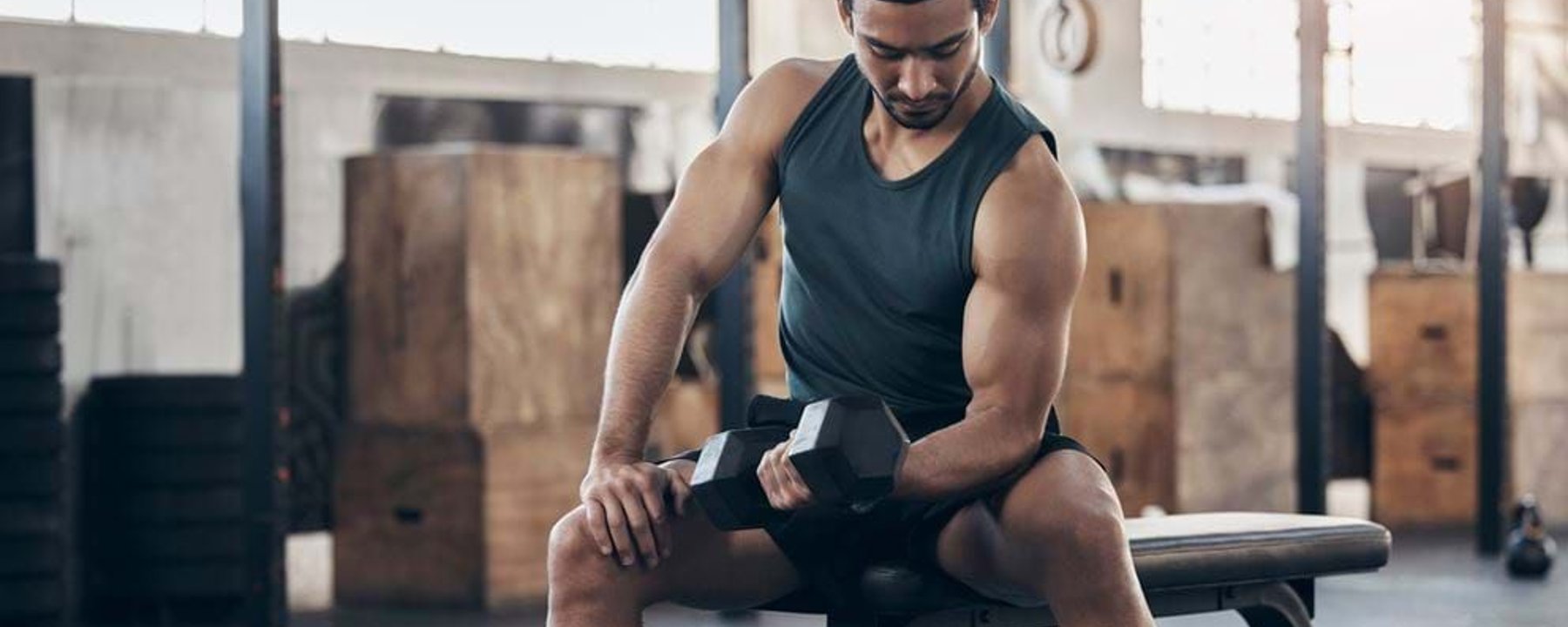 Man in black tank top lifting dumbbell while sitting on gym bench