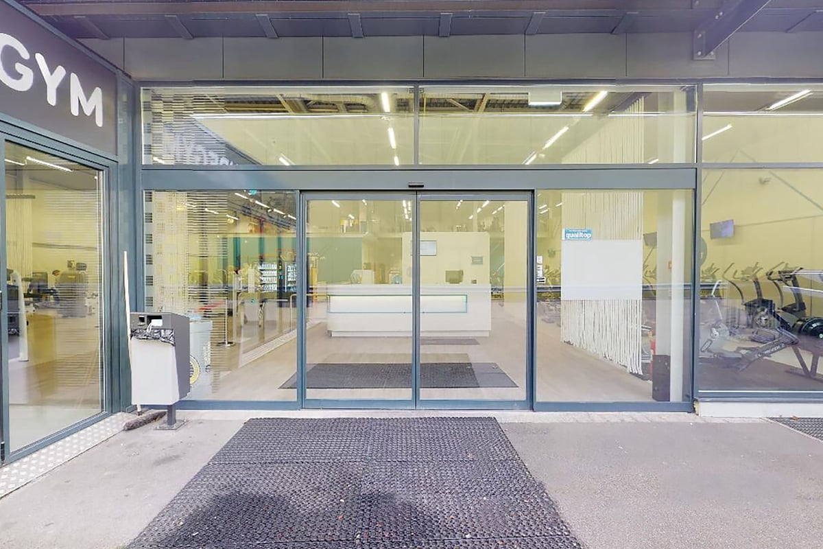 PureGym Oftringen: Gym entrance with glass doors, rubberized floor mat, exercise equipment visible inside the studio space.