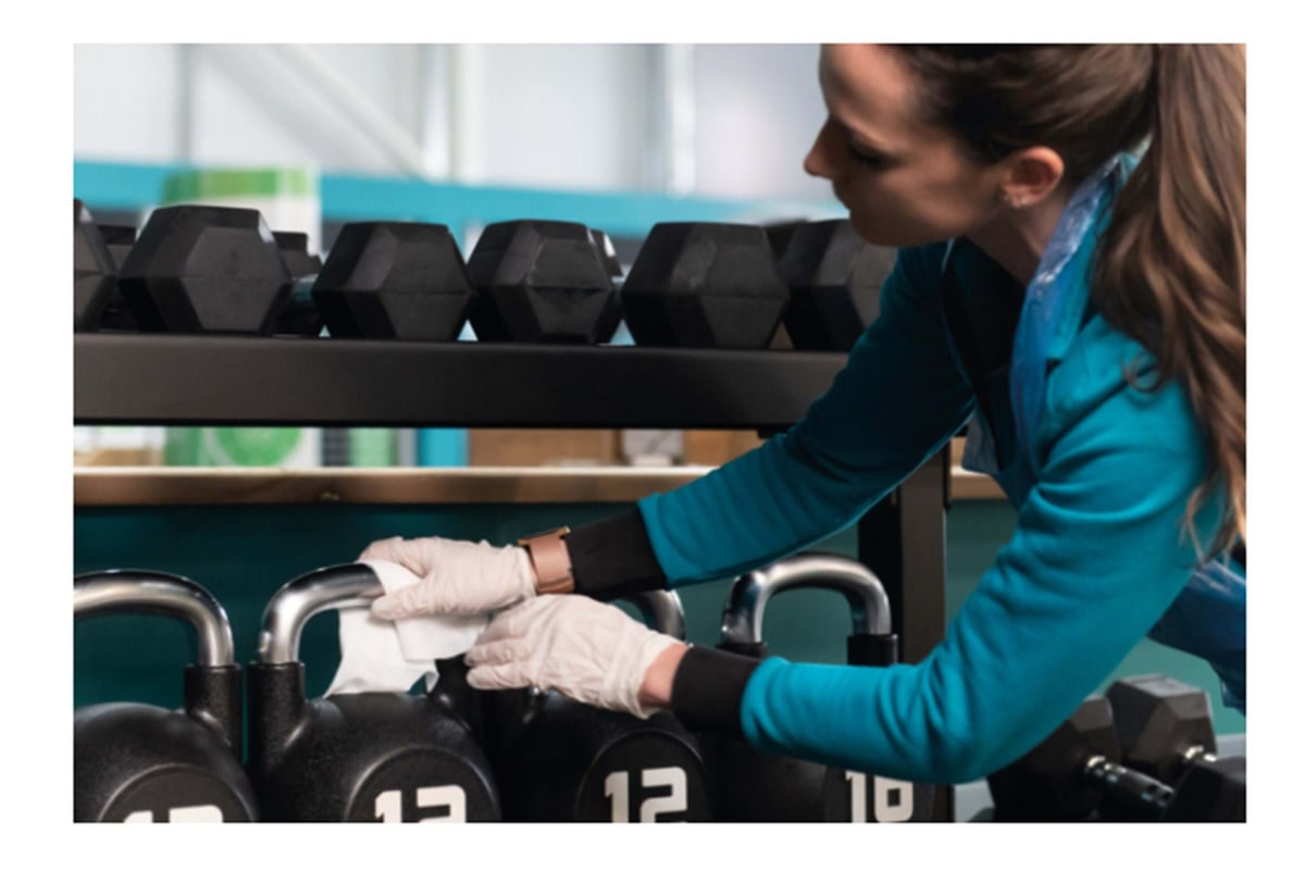 Team member wearing white gloves wiping down kettlebell in gym weights area