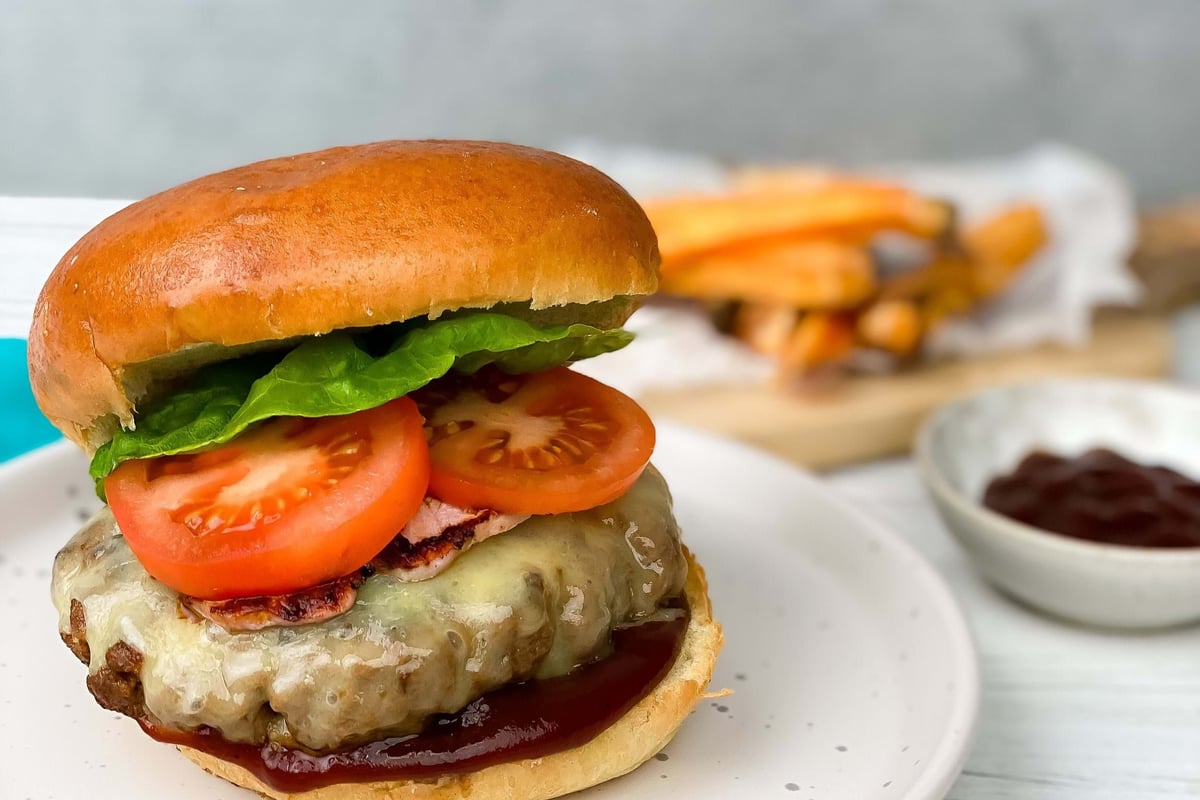 Cheeseburger with lettuce, tomato, and sauce on a white plate with fries and ketchup.