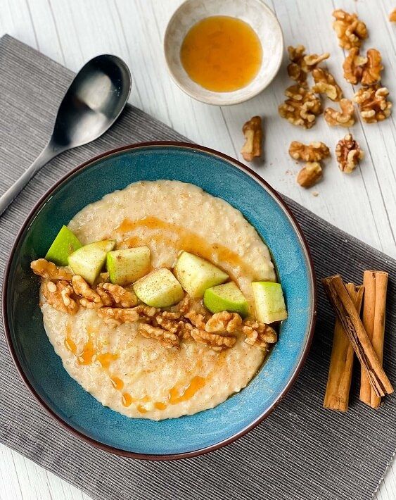 Porridge topped with walnuts, apple pieces, and honey drizzle in a blue bowl.