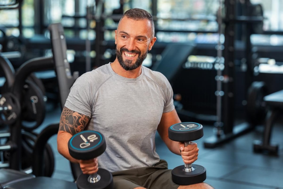 Smiling PureGym member sat down holding dumbbells