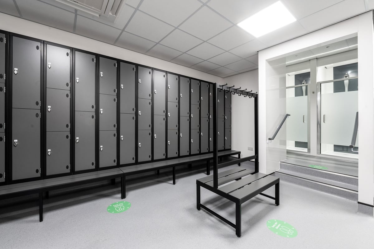 PureGym Witney: Row of lockers, benches in a changing room setting with showers visible.