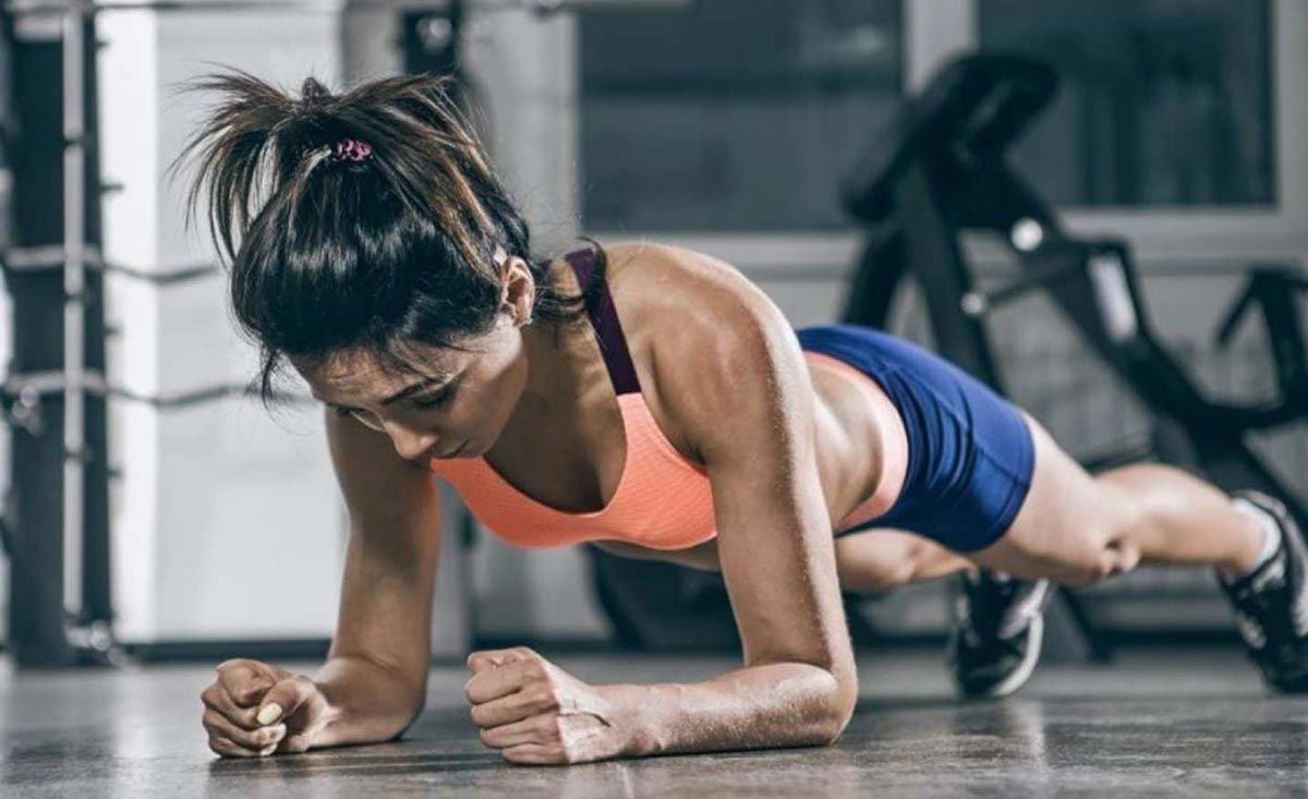 Frau in Sportkleidung macht Unterarmstütz auf dem Fitnessstudio-Boden