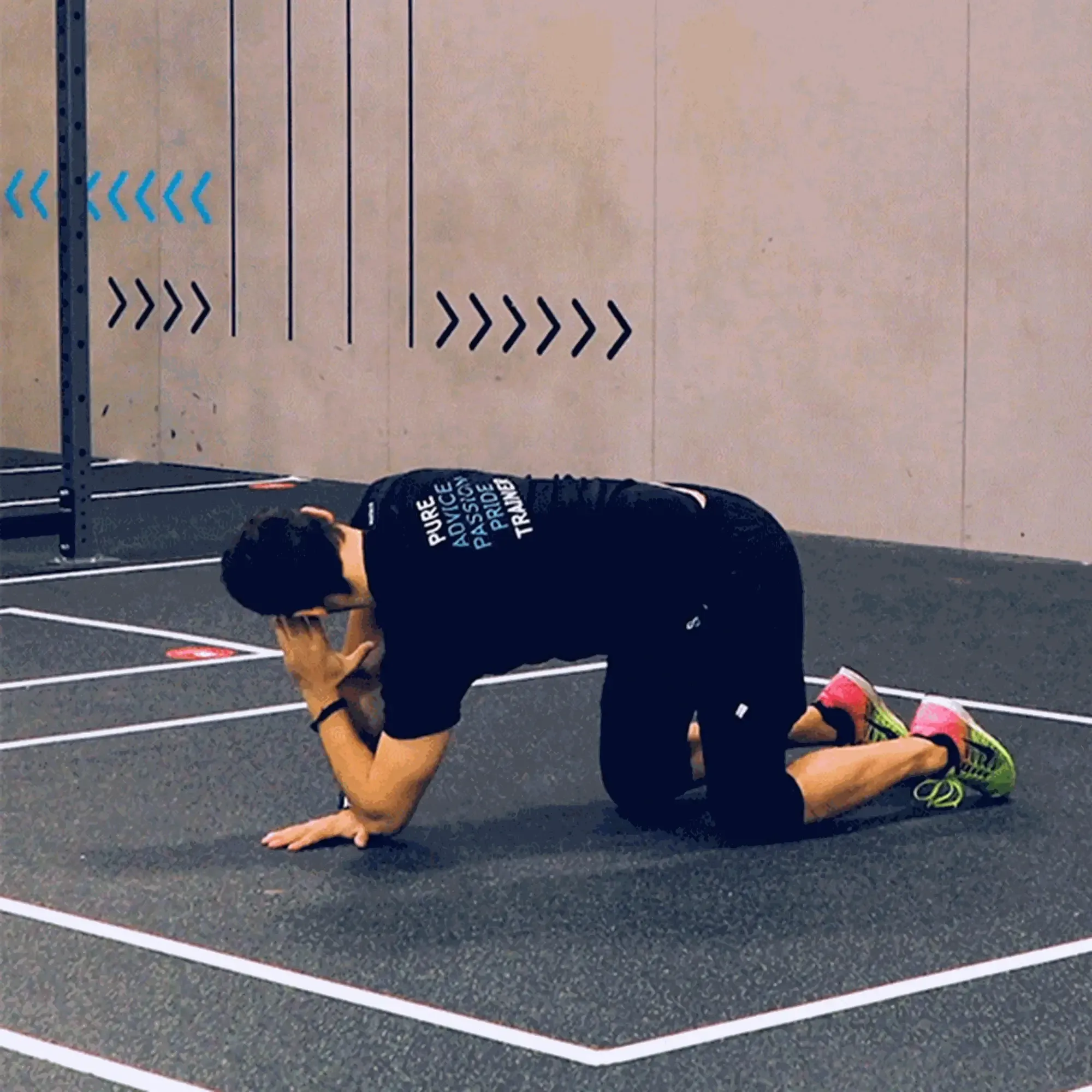 Man in black clothes and pink shoes doing a stretching exercise on gym floor
